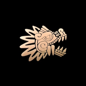 May include: A gold-colored, stylized illustration of a dragon's head against a black background. The dragon's head is depicted in profile, with intricate details and sharp teeth. The design has a cultural or historical theme.