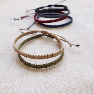 May include: Two braided bracelets, one in a light brown color and the other in a dark green color. The bracelets are stacked on top of each other. The text "an tam bracelets" is visible below the bracelets.