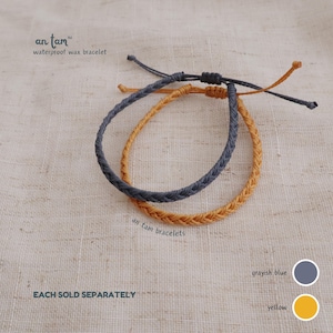 May include: Two braided waterproof wax bracelets, one greyish blue and one yellow. The bracelets have adjustable knots. The image text reads "an tam waterproof wax bracelet" and "an tam bracelets".