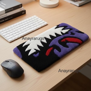 Peut inclure: Un tapis rectangulaire avec un motif inspiré des requins, avec des dents blanches, des accents violets, noirs et rouges. Le tapis est posé sur un bureau en bois à côté d'un clavier et d'une souris sans fil. Le texte "Anayrarugs" est visible.