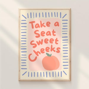 Puede incluir: Una impresión artística enmarcada con el texto "Take a Seat Sweet Cheeks" en letras naranjas. La impresión presenta una ilustración de melocotón y está rodeada por un borde amarillo claro con líneas verticales azules.