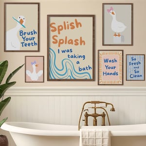 Puede incluir: Colección de arte mural enmarcados con temática de baño. El arte presenta ilustraciones de gansos y textos como "Brush Your Teeth", "Splish Splash" y "Wash Your Hands". La paleta de colores incluye beige, azul y naranja.