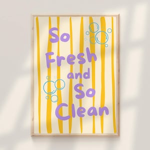 Puede incluir: Un estampado enmarcado con fondo crema y rayas verticales amarillas. El texto "So Fresh and So Clean" es de color púrpura, con ilustraciones de burbujas azules. El marco es de color madera clara.