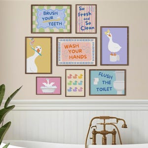 May include: A collection of framed bathroom art prints featuring cartoon geese and ducks. The prints include phrases like "Brush Your Teeth," "Wash Your Hands," and "Flush the Toilet." The color palette includes pastels and earth tones.