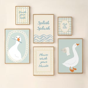 Può includere: Una collezione di quadri incorniciati a tema bagno. Le opere presentano illustrazioni di oche, testi come "Brush your Teeth" e "Please Wash your Hands", e motivi a onde in morbidi colori blu e crema.