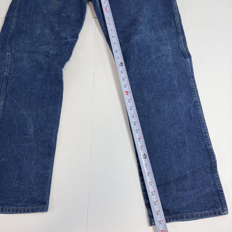 May include: Close-up of blue denim jeans with a measuring tape showing a length of approximately 79 cm. The jeans have a classic, straight-leg design and a faded wash, with visible wear marks.