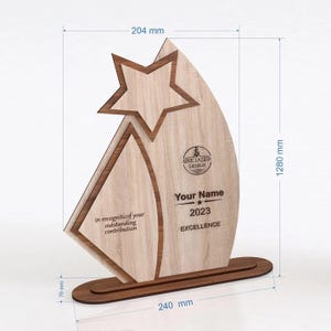 May include: Wooden award trophy with a star cutout and a curved design. The trophy is 1280 mm tall, 240 mm wide, and 70 mm thick. It features the text "Your Name", "2023", and "EXCELLENCE". The text "in recogniticof your outstanding contribution" is also visible.