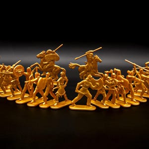 Puede incluir: Colección de soldados de juguete dorados, incluyendo infantería y caballería, dispuestos sobre una superficie negra. Las figuras están en varias poses, algunas a caballo con lanzas, otras a pie con escudos y armas.