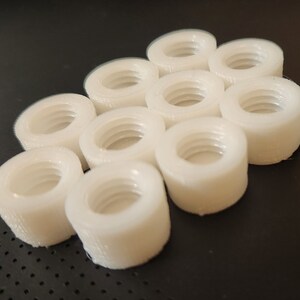 Puede incluir: Un grupo de 10 tuercas de pl&aacute;stico blanco, dispuestas en un patr&oacute;n hexagonal.