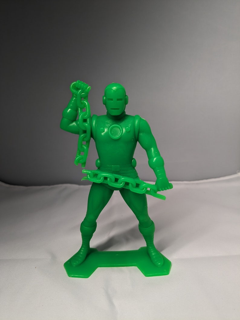 May include: Green plastic action figure of a superhero holding a chain in one hand. The figure is standing on a green plastic base.
