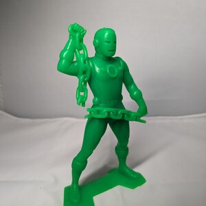 May include: Green plastic action figure of a superhero holding a chain in one hand. The figure is standing on a green plastic base.