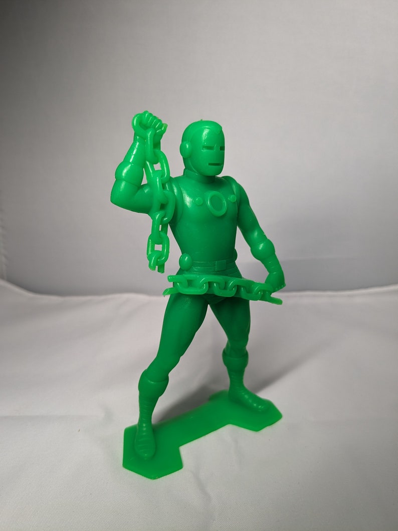May include: Green plastic action figure of a superhero holding a chain in one hand. The figure is standing on a green plastic base.
