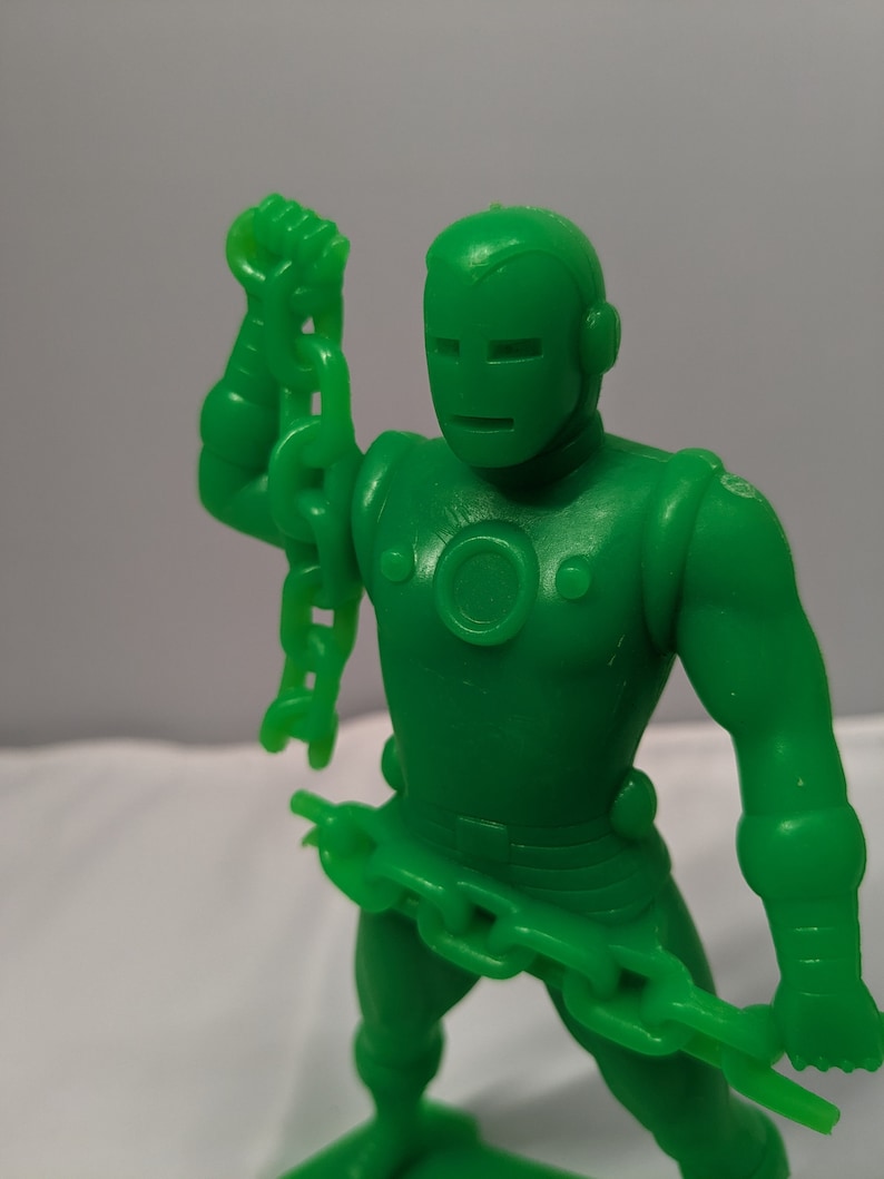 May include: Green plastic action figure of a superhero holding a chain in each hand. The figure has a metallic look and a helmet with a face mask.