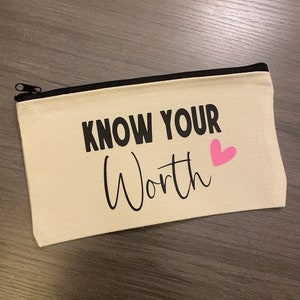 Könnte beinhalten: Rechteckiges Federmäppchen aus beigem Canvas mit schwarzem Reißverschluss. Der Text "KNOW YOUR Worth" ist in Schwarz mit einem rosa Herz aufgedruckt. Praktisches Accessoire.