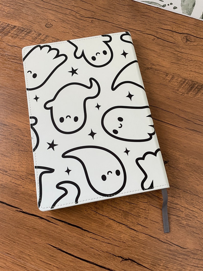 May include: A white notebook with a black and white ghost pattern. The notebook has a black ribbon bookmark.