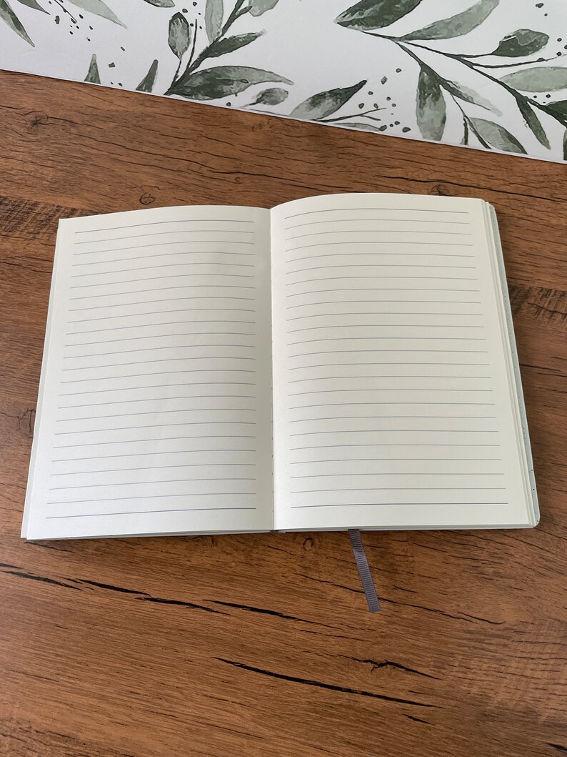 May include: An open lined notebook with a gray bookmark. The notebook is lying flat on a wooden surface.