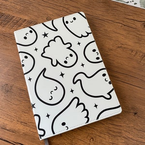 May include: A white notebook with a black and white ghost pattern. The notebook has a grey ribbon bookmark.