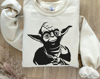 Peut inclure: Un sweat-shirt beige avec un motif noir et blanc de Yoda de Star Wars. Le motif est centré sur le devant du sweat-shirt.