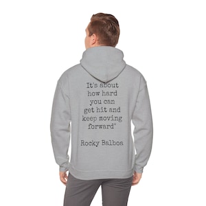 May include: A light gray hoodie with the quote "It's about how hard you can get hit and keep moving forward" attributed to Rocky Balboa printed on the back. The hoodie has a hood and a relaxed fit.