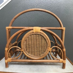 May include: A woven rattan magazine rack with a circular woven design in the center. The rack has a curved top and stands on four legs.