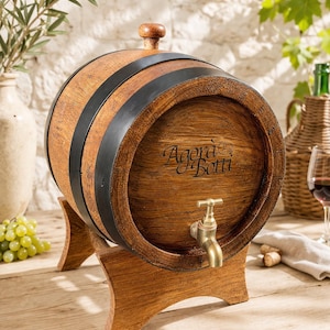 Peut inclure: Un tonneau à vin en bois avec des cercles en métal noir et un robinet en laiton. Le tonneau est monté sur un support en bois et porte l'inscription "Agora Botti". L'arrière-plan comprend un verre de vin, des raisins et un vase décoratif.