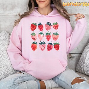 Pode incluir: Moletom rosa com estampa gr&aacute;fica de morangos em v&aacute;rios tons de vermelho e rosa.