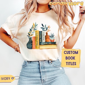 May include: A white t-shirt with a graphic of a bookshelf with books and plants. The books have the text "Book Title 1", "Book Title 2", and "Book Title 3" on the spines. The text "CUSTOM BOOK TITLES" is on a yellow background in the lower right corner of the image.