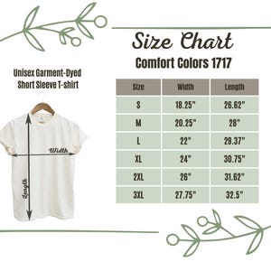 Op de afbeelding: Cr&egrave;mekleurig unisex garment-dyed T-shirt met korte mouwen op een hanger. Een maattabel toont afmetingen in inches voor maten S tot 3XL, inclusief breedte en lengte. De tabel is gelabeld "Comfort Colors 1717".
