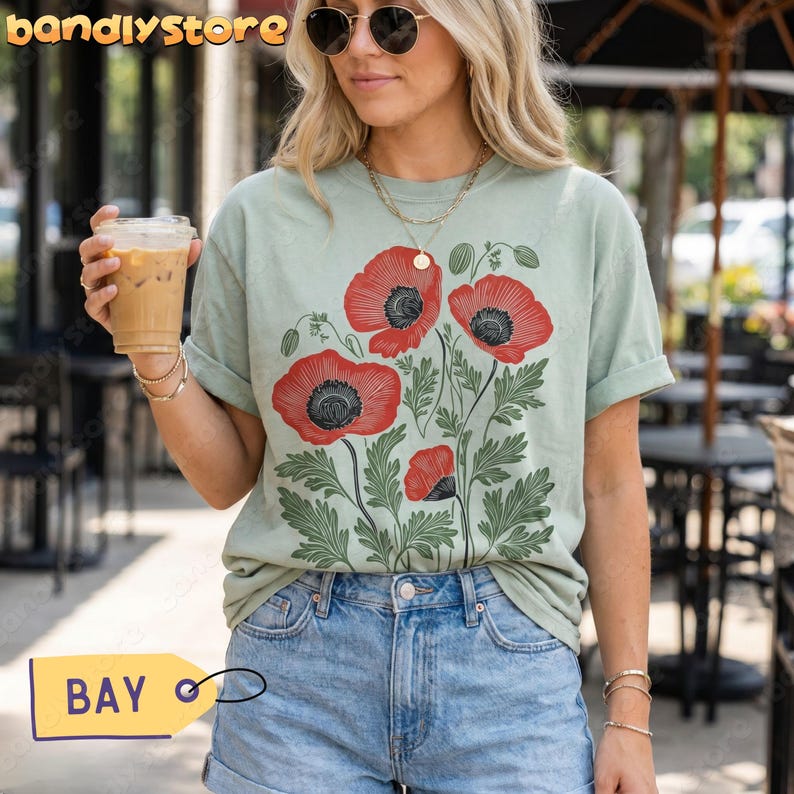 May include: A sage green t-shirt with a bold floral print of red poppies with black centres and green leaves. The shirt is worn with denim shorts. The image includes the text "bandlystore" and a yellow tag that says "BAY".