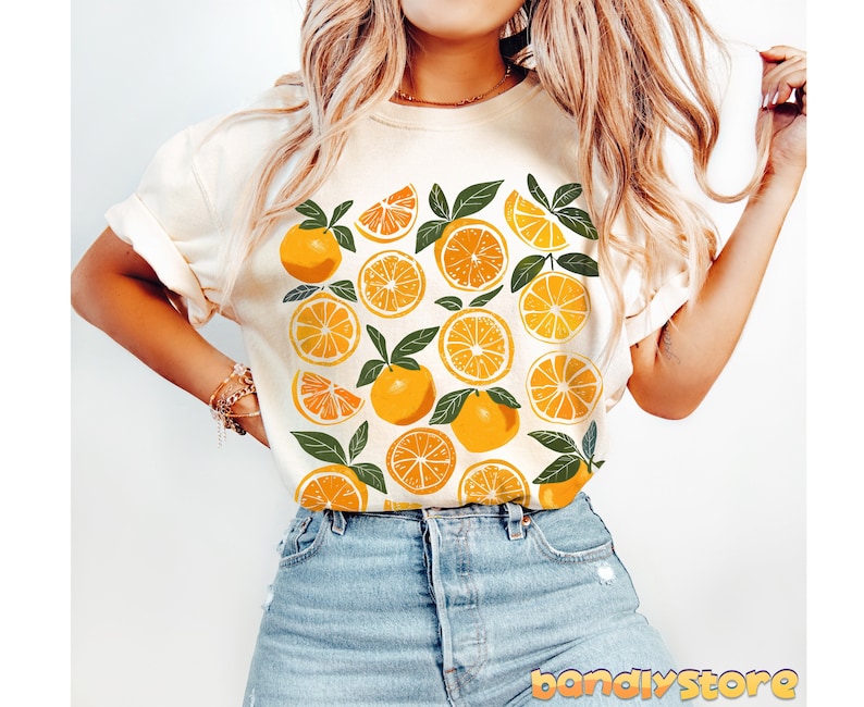 May include: A white t-shirt with a graphic print of orange slices and green leaves. The shirt is a casual style with a crew neck and short sleeves.