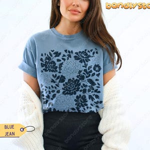 Op de afbeelding: Een blauw spijkerbroekkleurig t-shirt met een donkerblauw bloemmotief. Het shirt heeft korte mouwen en een ronde hals. Het label op het shirt zegt "BLUE JEAN".