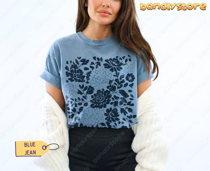 Op de afbeelding: Een blauw spijkerbroekkleurig t-shirt met een donkerblauw bloemmotief. Het shirt heeft korte mouwen en een ronde hals. Het label op het shirt zegt "BLUE JEAN".