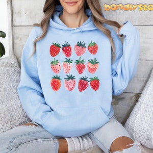 Pode incluir: Um moletom azul claro com um gr&aacute;fico de morangos em tons de rosa e vermelho. Os morangos est&atilde;o dispostos em uma grade.