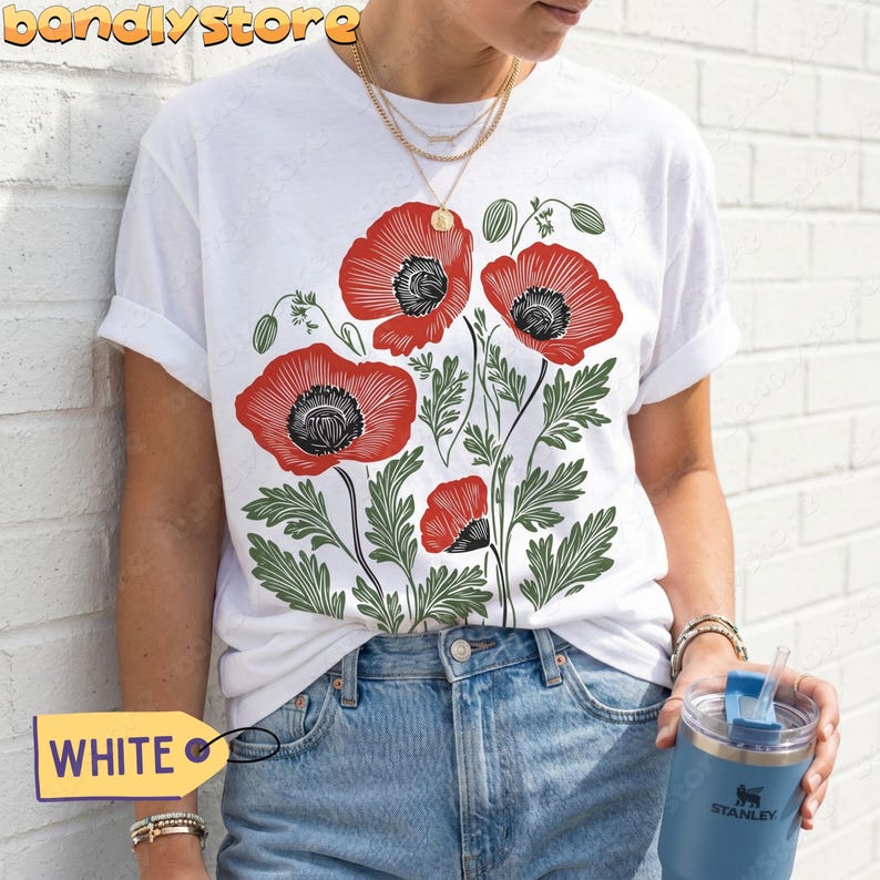 May include: White t-shirt with a bold floral print of red poppies, black centers, and green foliage. The design is centrally placed. A yellow tag displays the word "WHITE".