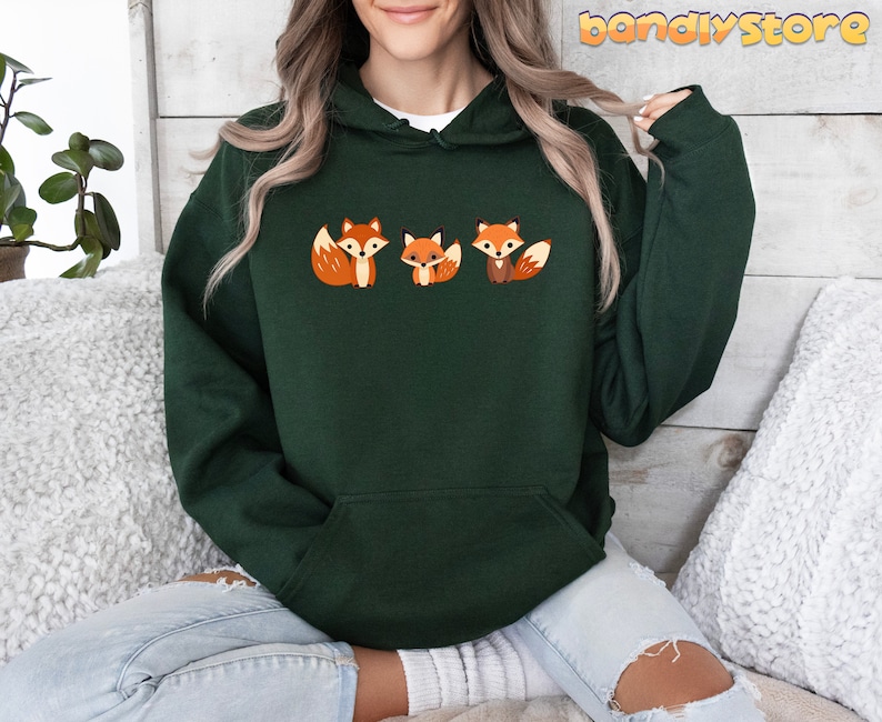 May include: A dark green hooded sweatshirt with a graphic of three cartoon foxes. The foxes are orange and white with black eyes and noses.