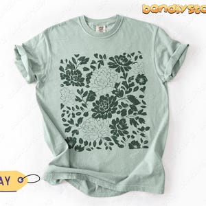 Flat-lay of a sage green (Bay) shirt with a deep green linocut flower design, neatly folded on a white background.
