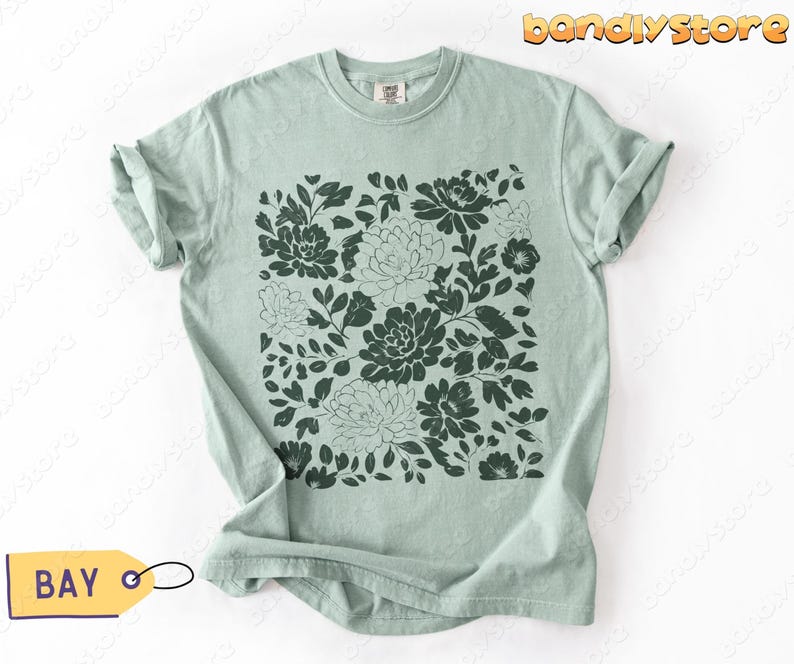 Flat-lay of a sage green (Bay) shirt with a deep green linocut flower design, neatly folded on a white background.