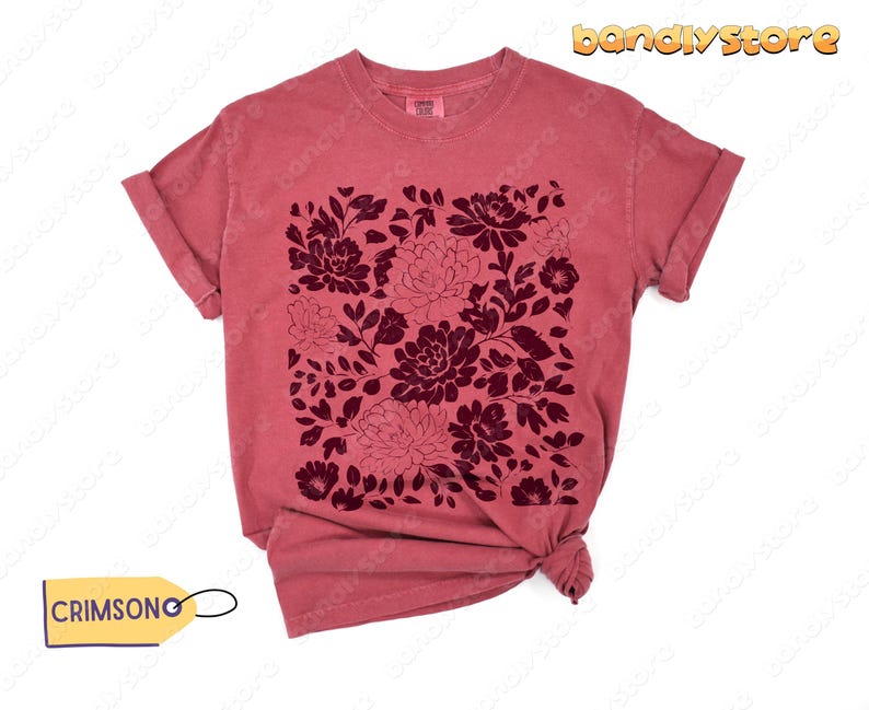 Op de afbeelding: Een stoffig roze t-shirt met een donker bordeauxrood bloemmotief. Het bloemmotief is een vierkante opstelling van verschillende bloemen en bladeren. Het shirt heeft opgerolde mouwen en een knoop aan de onderkant. Het label zegt "CRIMSONG".