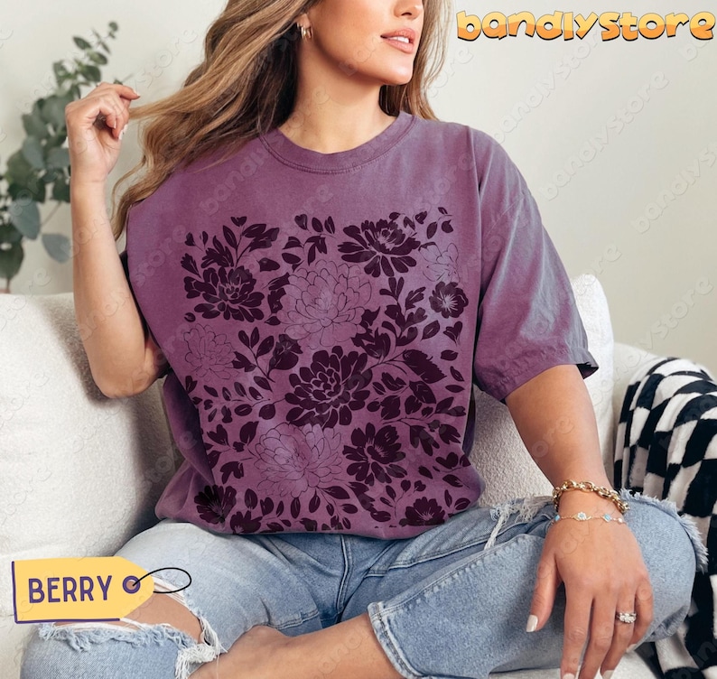 Woman in a muted purple (berry) tee featuring deep plum linocut flowers. The shirt has a cozy, relaxed cottagecore feel.