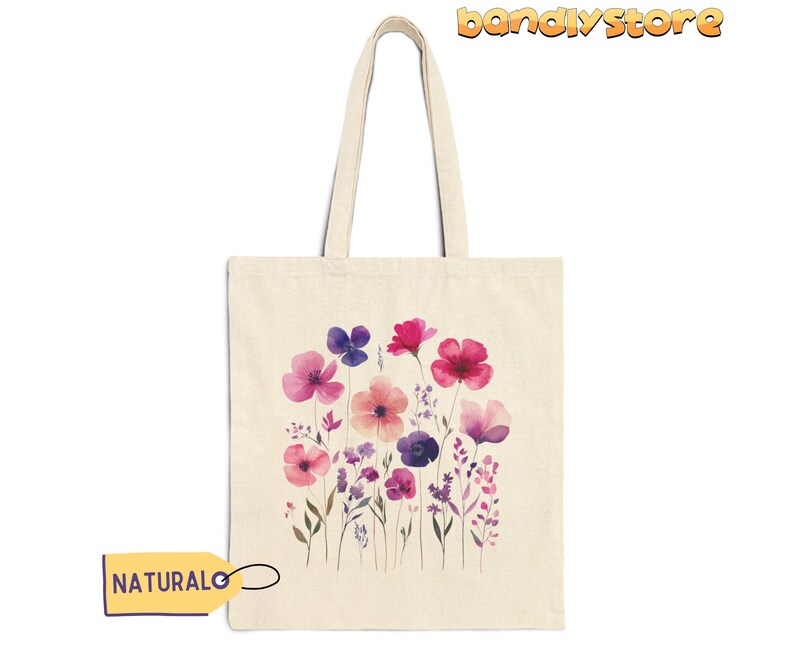 May include: A natural canvas tote bag with a design of watercolor pink, purple, and white flowers. The bag has a natural fabric handle.