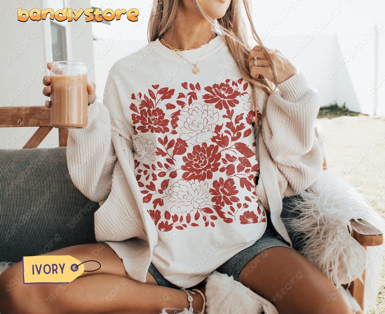 Woman wearing an ivory Comfort Colors tee with reddish-brown linocut-style flowers and leaves. The design has a handmade vintage stamp effect.