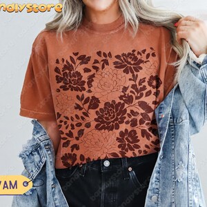 Woman in a rich yam orange tee showcasing a rustic dark red linocut floral print, styled with a denim jacket and black jeans.