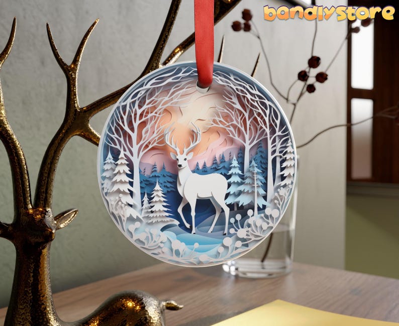 May include: White papercraft ornament featuring a deer standing in a snowy forest scene. The ornament is round and has a blue and white color scheme.