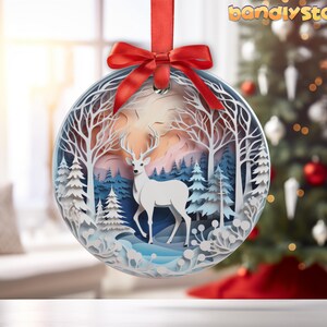 May include: A white papercraft ornament featuring a white deer standing in a snowy forest scene. The ornament is round and has a red ribbon attached to the top.