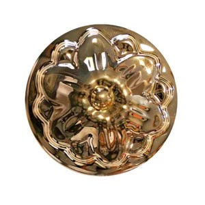 Peut inclure: Un bouton métallique doré de forme circulaire présentant un motif floral en relief avec cinq pétales arrondis rayonnant autour d'un dôme central. La surface possède une finition polie et réfléchissante qui capte la lumière.