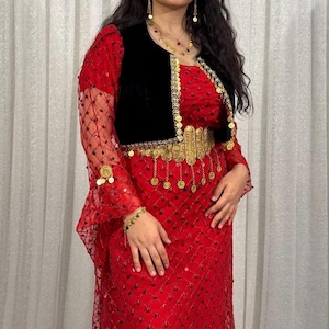 Könnte beinhalten: Ein bodenlanges rotes Kleid mit einem transparenten Überwurf im Rautenmuster und kleinen dunklen Verzierungen. Das Kleid enthält eine schwarze Samtweste, die mit einem goldfarbenen Metallgürtel mit hängenden Münzakzenten verziert ist.