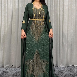 Könnte beinhalten: Ein bodenlanges, dunkelgrünes Kleid mit langärmeligem Überwurf, verziert mit aufwendigen goldfarbenen Stickereien und Pailletten. Das Kleid ist mit einer passenden goldfarbenen Kettenhalskette und einem Gürtel versehen, die über das Oberteil fallen.