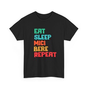May include: Black t-shirt with the words "EAT SLEEP MICI BERE REPEAT" in green, blue, orange, yellow, and red block letters. The shirt is a crew neck style.