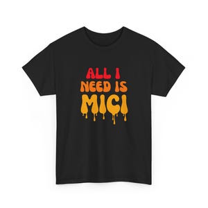 May include: Black t-shirt with the text "ALL I NEED IS MICI" in red and orange dripping font. The shirt is a short-sleeved crew neck style.