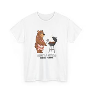 May include: White t-shirt featuring a cartoon bear wearing a red and white checkered apron, grilling food on a small barbecue. The text "URSU' LA GRĂTAR MICI CU MUSTAR" is printed below the bear.